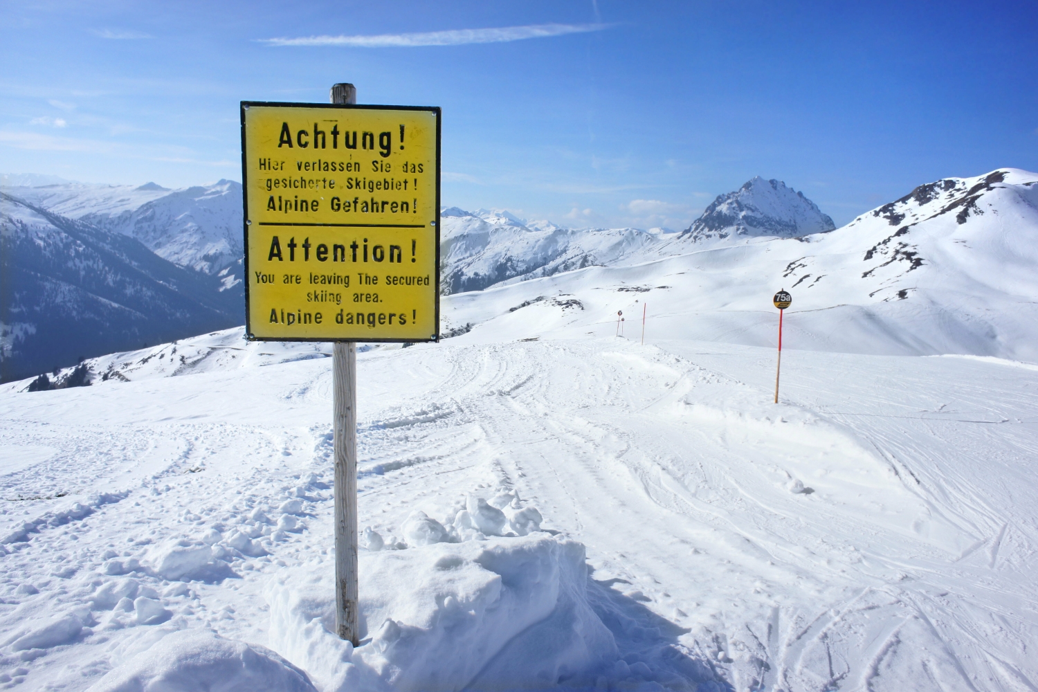 Auf dem verschneiten Berg steht ein Warnungsschild "Achtung hier verlassen Sie das gesicherte Skigebiet! Alpine Gefahren!